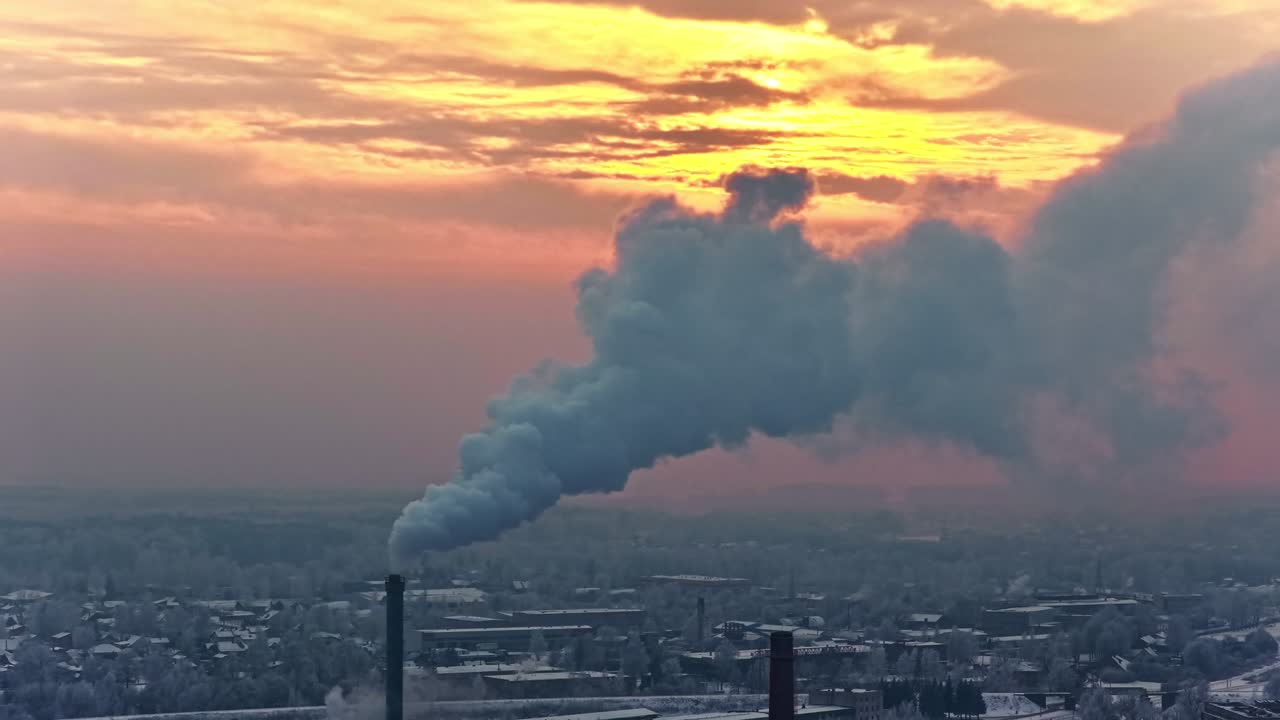 Ciminiera di una fabbrica che emette fumo alla periferia di una città al tramonto