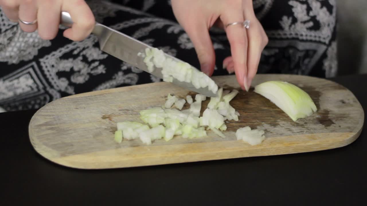 A woman's hands chopping a onion on a wooden cutting board with a sharp knife, static close up
