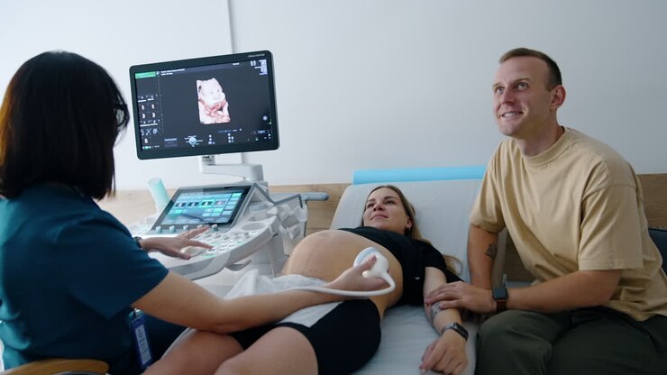 Caucasian expecting couple a diagnosed at ultrasound equipment. Smiling happy people looking at their future baby on the monitor.