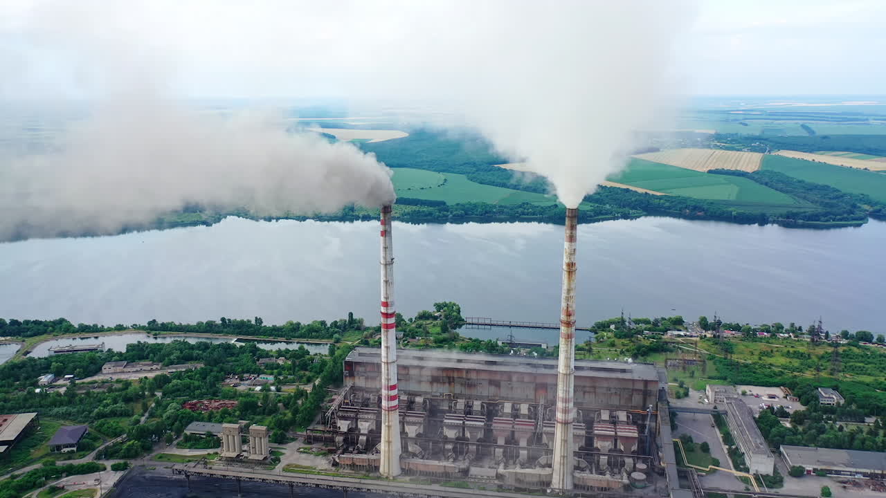 Drone shot of industrial zone with thick smog and burning fossil fuels. Factory zone pan shot left to right of polluted city, many factory chimneys in city area