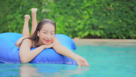 Beautiful-Young-Girl-Floating-On-A-Mattress-in-swimming-pool,-facing-camera-and-she-is-laying-on-her-tummy
