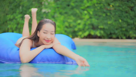 beautiful young girl floating on a mattress in swimming pool, facing camera and she is laying on her tummy