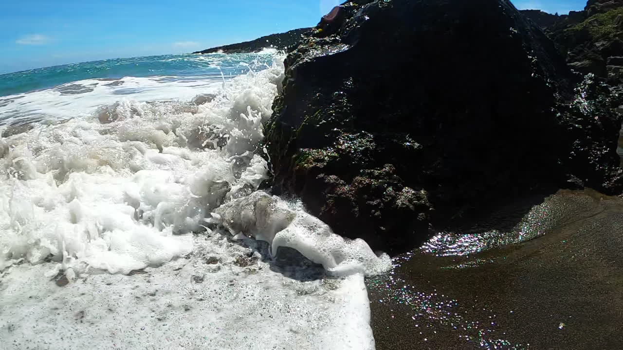 la ola choca contra la roca en la costa de la playa de arena verde