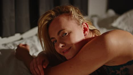 portrait of pretty woman in lingerie sensually laying down in bed while looking at camera in slow motion