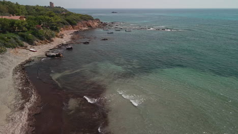 vista de la cala con mar transparente y tranquilo cerca de la costa con vegetación verde en cerdeña, italia - tiro estático aéreo