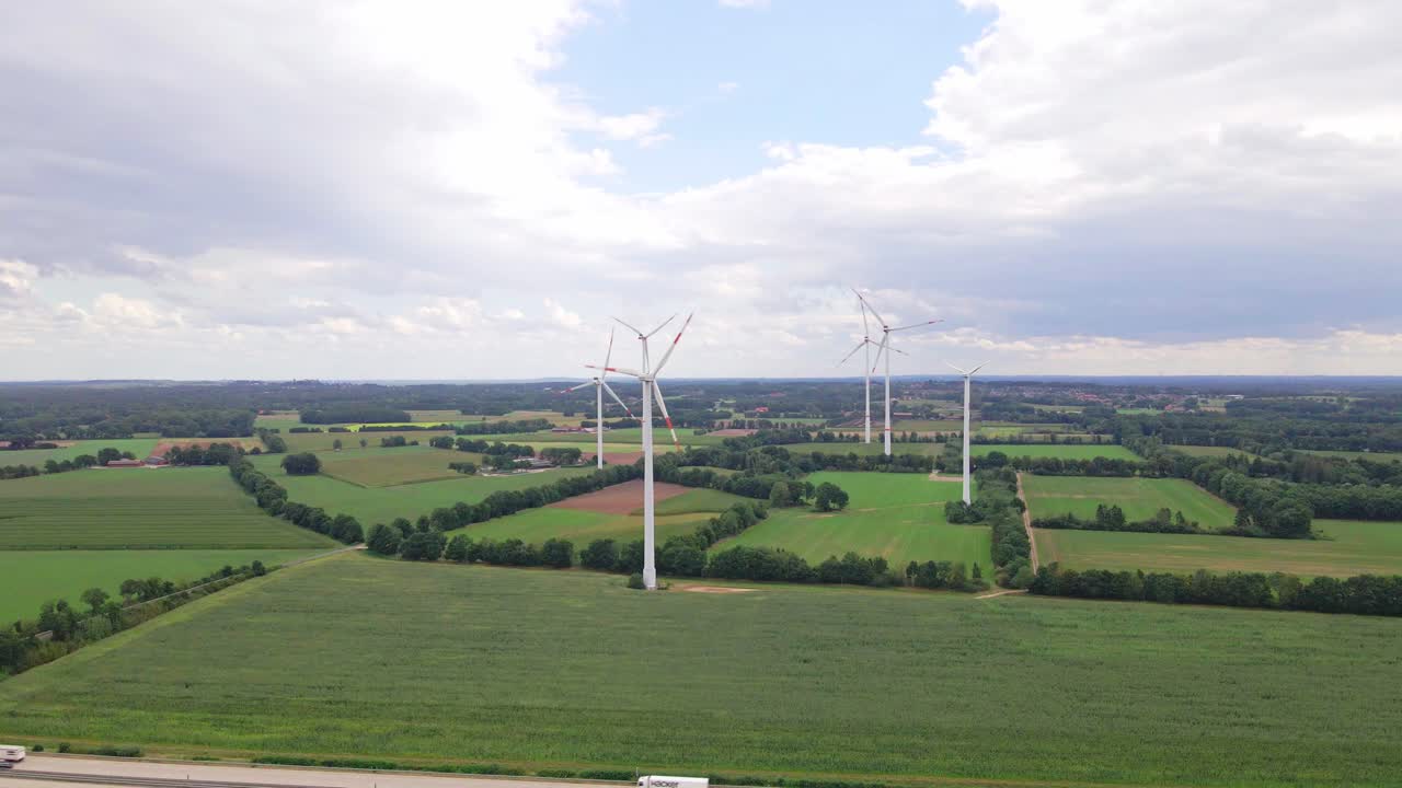 Drone footage of wind turbines beside a highway, surrounded by farmland and cornfields