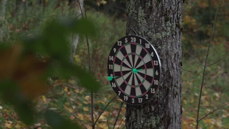 Darts fly through the air and hit a dart board in slow motion