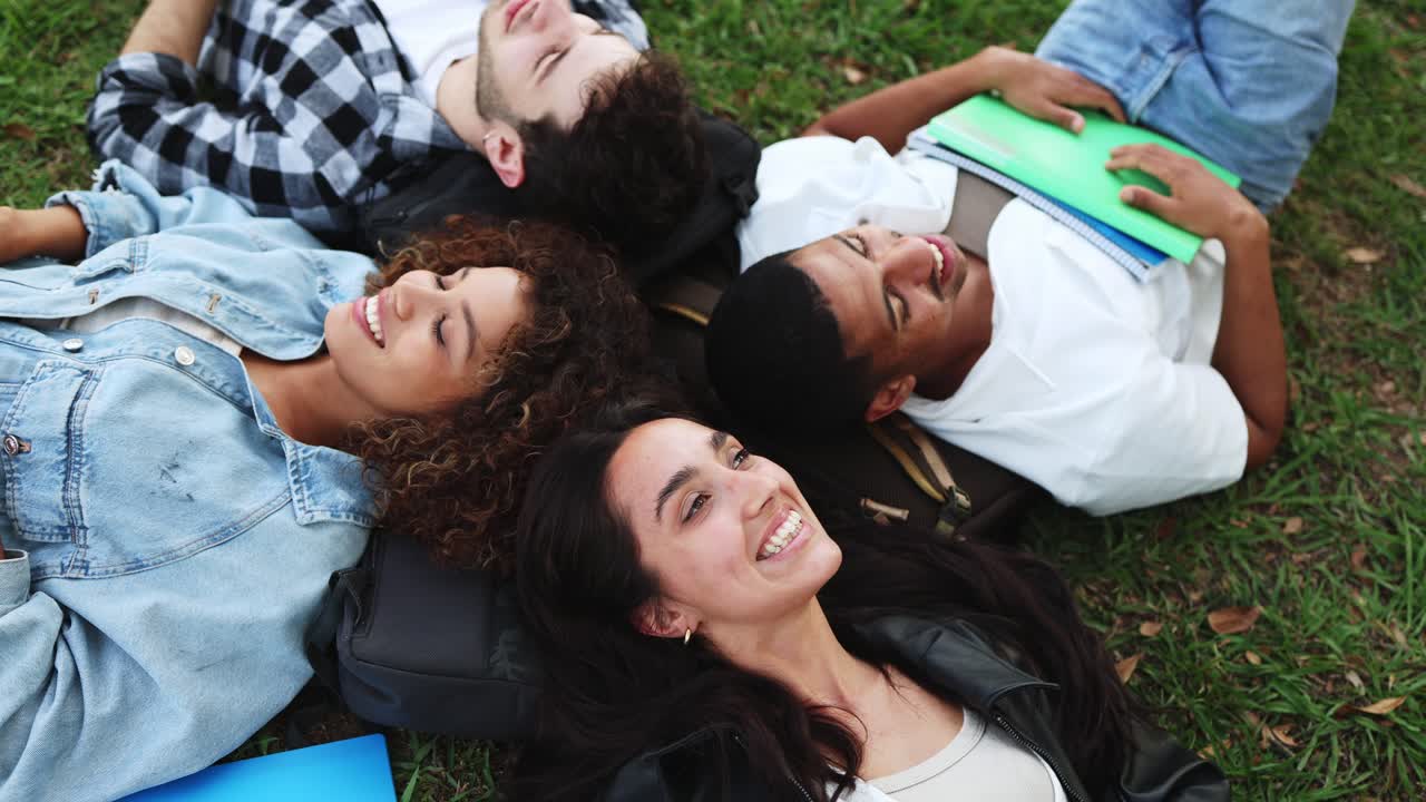 Studenti felici di diverse etnie sdraiati sull'erba che ridono insieme.