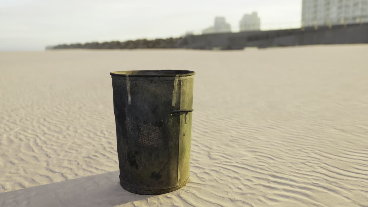 Discarded trash can stands alone on the sandy beach at sunrise