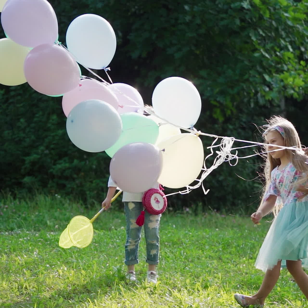 Happy girls with balloons in the park. Soap bubbles flying in the air and little children enjoying time together outdoors in summer.