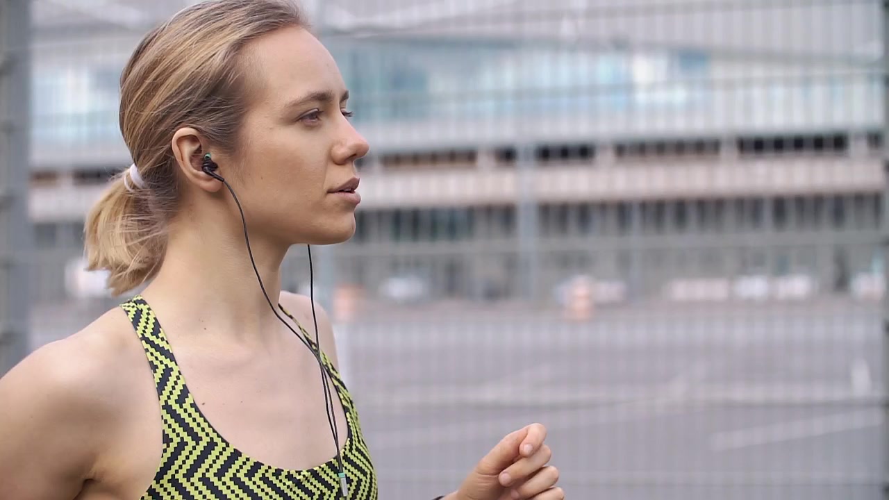 Mujer joven trotando en el sitio con auriculares en un entorno urbano