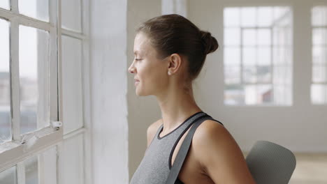 healthy caucasian woman ready for yoga exercise looking out window planning ahead enjoying healthy lifestyle in fitness studio