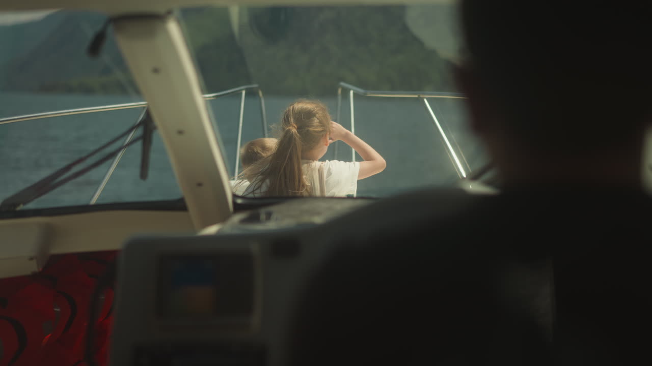 Little girl and junior brother sit on sailboat bow deck view from skipper cockpit. Cute children observe seascape sailing yacht on summer vacation