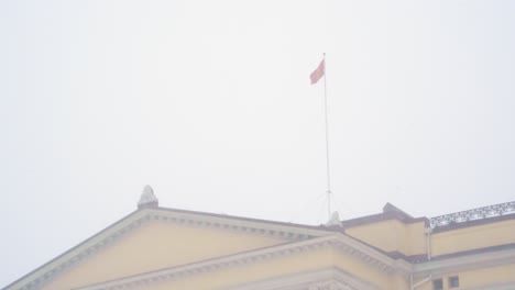 norwegian national flag flying above the royal palace in oslo during heavy snow