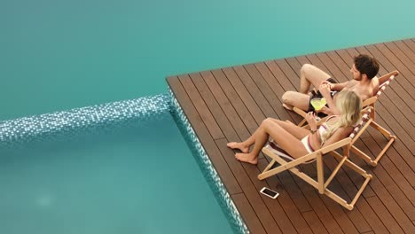 Cheerful-couple-drinking-cocktails-on-poolside-near-luxury-house.