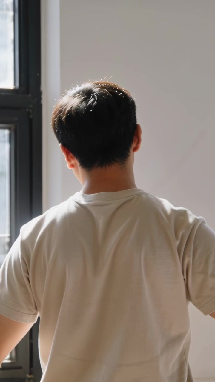 Vertical video: Lowering arms stretching man in beige tee rotating and turning head at home window
