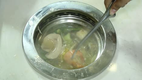 shrimps and vegetables cooking in broth in asian soup kitchen, closeup