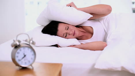 exhausted woman lying on her bed covering her ears