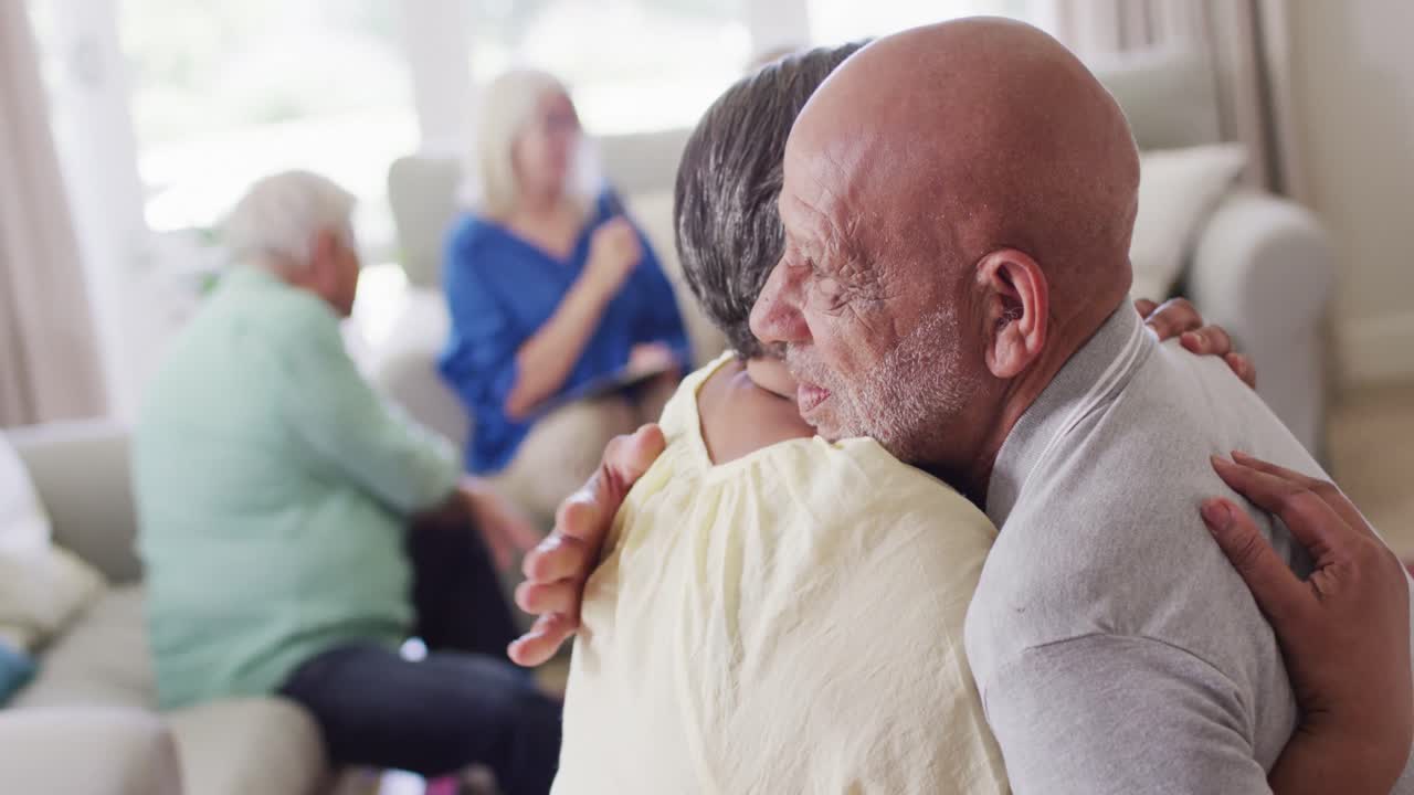 지원 그룹에서 슬픈 다양한 시니어 여성 친구를 포옹하는 시니어 바이라시안 남자, 느린 동작