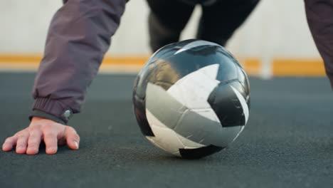 close up of partial view of athlete performing push-ups alternating hand placement on soccer ball demonstrating strength outdoor urban ground