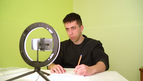 Left-handed-Man-Taking-Notes-During-Online-Course-Via-Mobile-Phone-Camera-With-Ring-Light