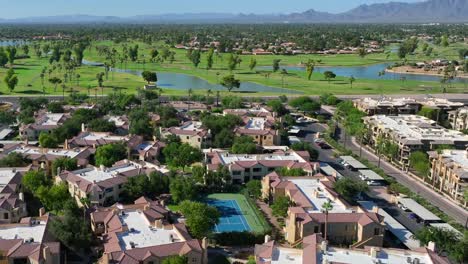 Vista-Aérea-Del-Suroeste-De-EE.UU.:-Exuberantes-Campos-De-Golf,-Fuentes-De-Agua-Y-Residencias-Con-Techo-De-Terracota,-Con-Un-Telón-De-Fondo-Montañoso-Y-Un-Cielo-Azul-Claro