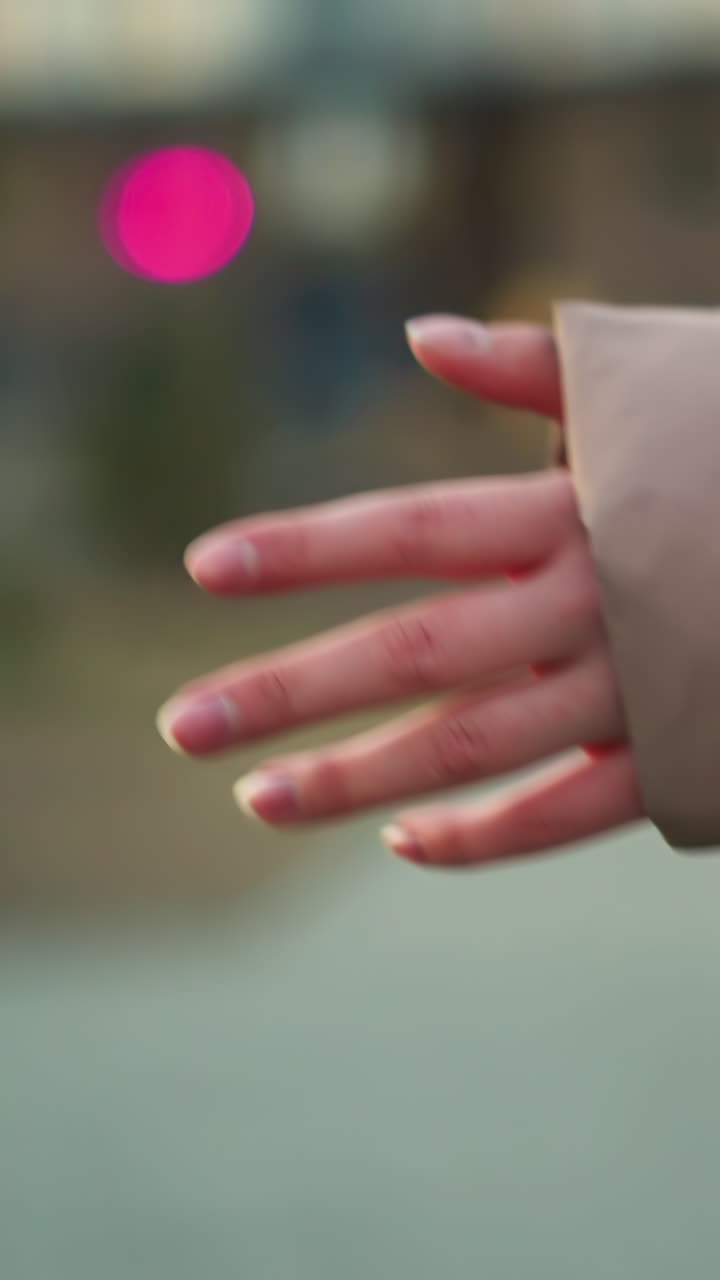 una toma de primer plano de la mano de una persona extendida frente a un fondo urbano borroso, con iluminación suave y efectos bokeh. la mano, vestida con una chaqueta de melocotón, es el foco principal