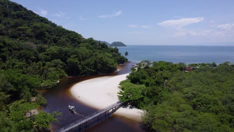 aerial view of a boat driving in the rio sahy river towards the sea in sunny brazil