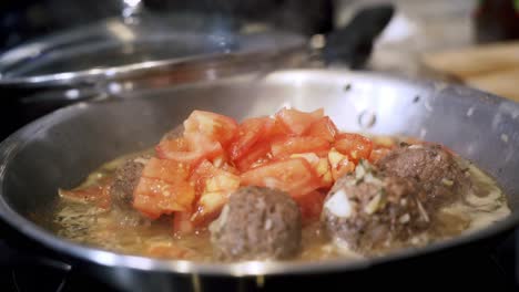 adding and cooking tomatoes in steel pan full of beyond meatballs preparing ingredients to make vegan beyond meatballs with spaghetti and meat sauce