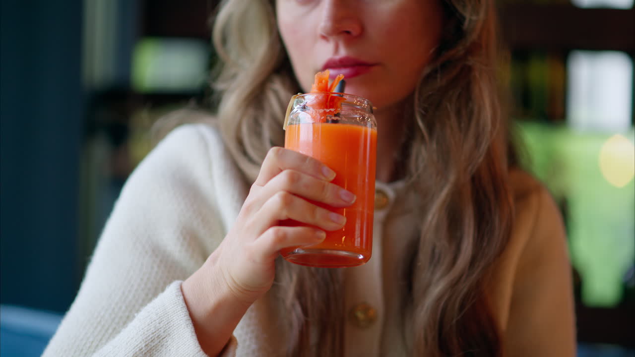 Woman drinking carrot juice using of a straw, at a restaurant