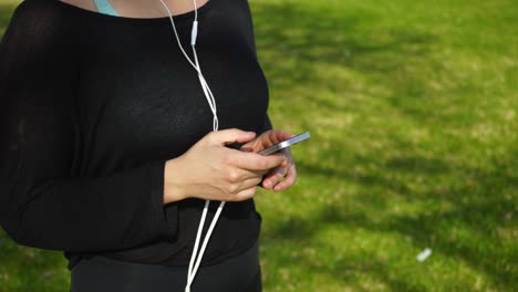 Sección-Intermedia-De-Una-Mujer-Joven-En-Ropa-Deportiva-Usando-Un-Teléfono-Inteligente-En-El-Parque