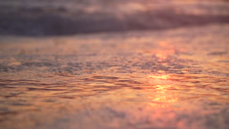 cierre en cámara lenta de una pequeña ola corriendo hacia el océano en la playa con burbujas al atardecer