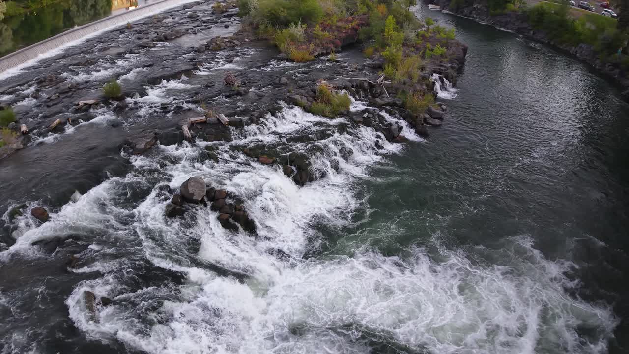 Et lille vandfald kaskaderer ned over klipper i en klar flod, der skaber hvidvandsstrømme i naturlige omgivelser.