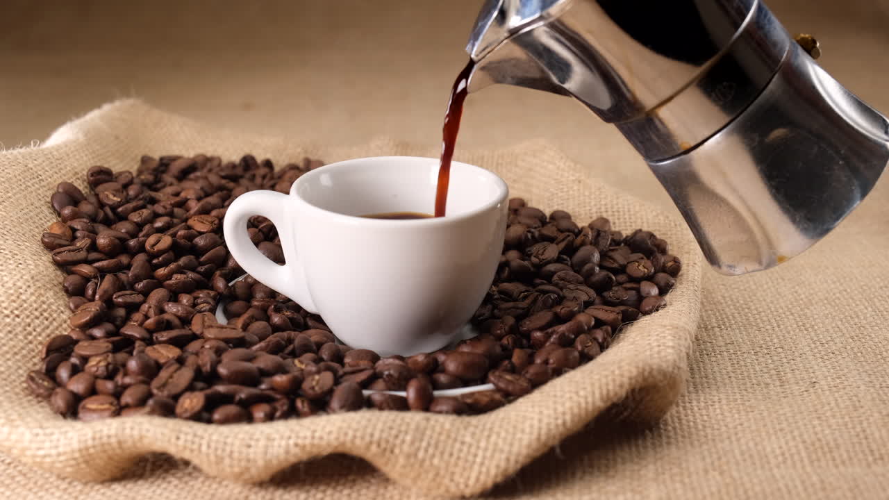 Pouring coffee cup from moka coffee machine on jute and coffee beans