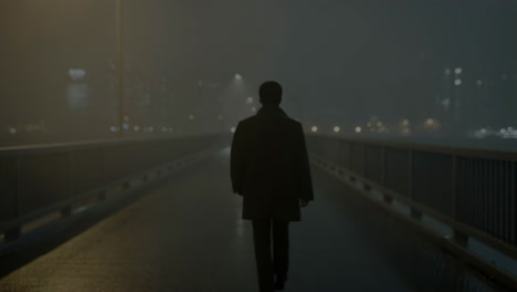 man walking alone on a foggy bridge at night