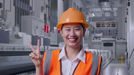 close up of asian female engineer with safety helmet smiling and showing peace gesture at pharmaceutical factory, vaccine production facility