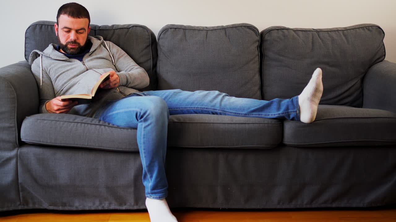 Man Reading Book While Sitting On The Couch In His Apartment