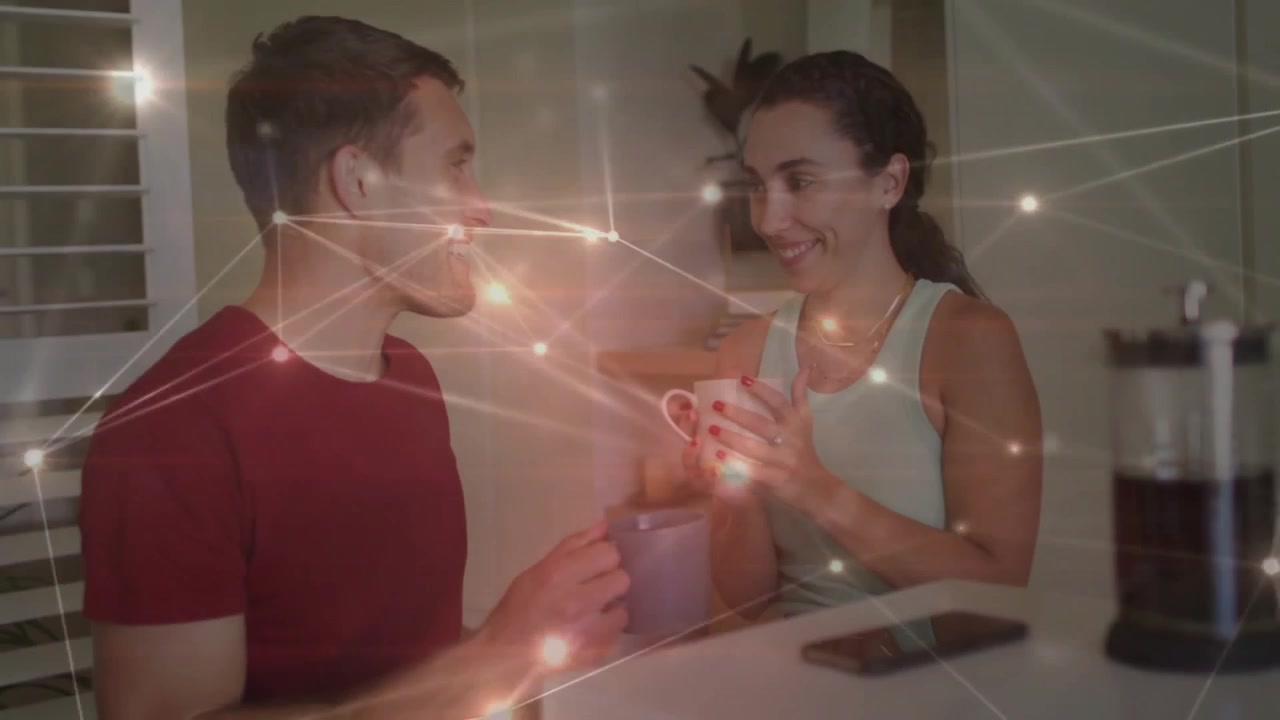 Uomo e donna che condividono un caffè in cucina, alzando le tazze e creando una sovrapposizione tecnologica che segnala un legame emotivo.