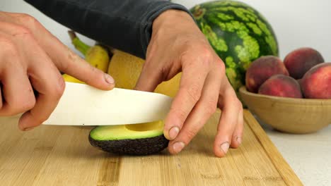 cortar un aguacate con un cuchillo de cerámica afilado, sobre una tabla de cortar de madera.