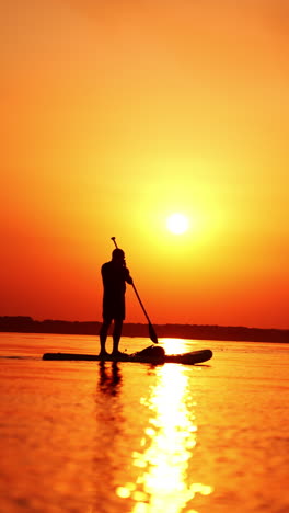 male figure standing on the sup board on calm river. man spending time on water at sunset in summer. vertical video