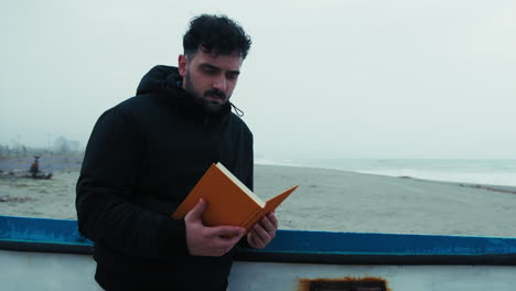 man carefully reads a book while relaxing by the sea in winter