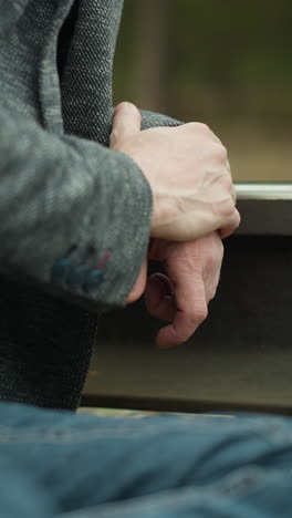 a close-up view of a man's hands clasped together, resting on a railway track. he is wearing a grey blazer and blue jeans