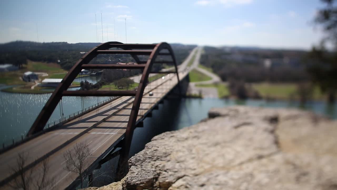 Austin Pennybacker Bridge, focus tilted to highlight narrow segment of ledge - front part of bridge. Traffic moving smoothly, bicyclist seen riding north on the bridge.