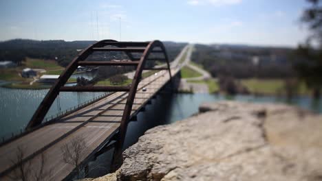 austin pennybacker bridge, focus tilted to highlight narrow segment of ledge - front part of bridge. traffic moving smoothly, bicyclist seen riding north on the bridge.