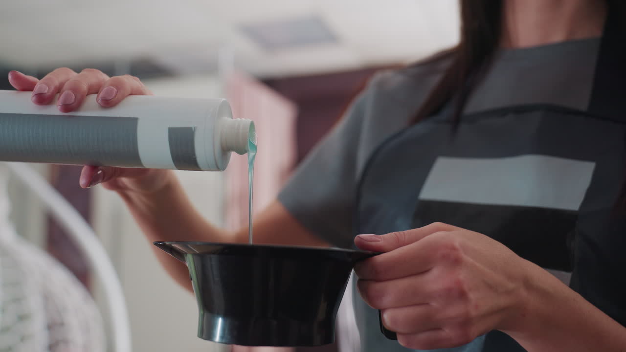 백인 컬러리스트가 밝은 살롱에서 믹싱 볼에 신중하게 developer를 붓고 있으며, 클로즈업된 손과 병, 정확한 측정이 보이고, 집중된 기술과 제품 텍스처가 눈에 띄는 전문적인 모습이에요.