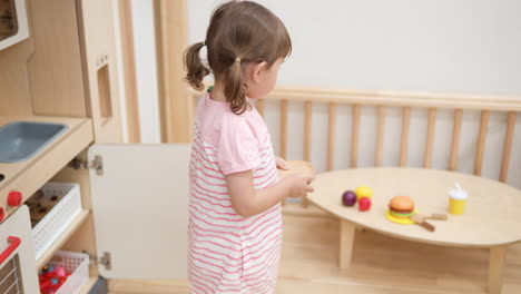 una niña juega en su cocina de juguete, coloca platos con frutas en una mesa de madera - cámara lenta