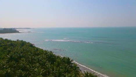 Aerial-view-of-vast-turquoise-ocean-water-and-green-palm-tree-forest-in-a-tropical-island