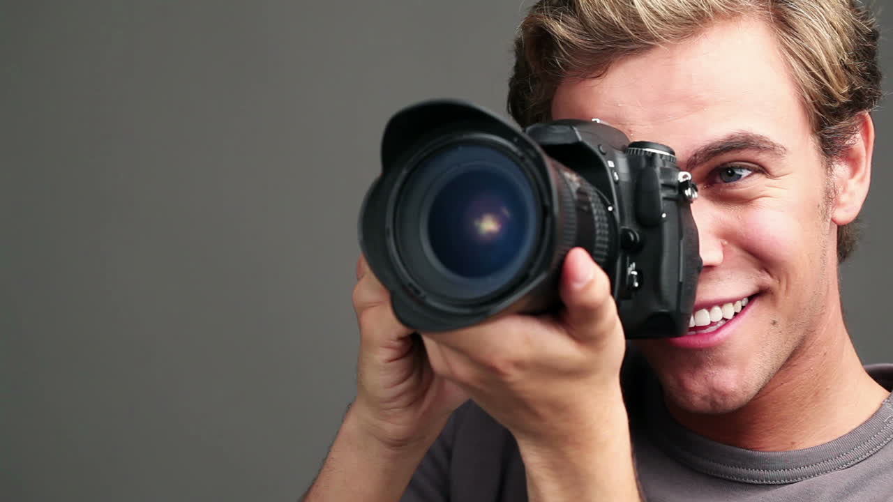 giovane uomo che tiene in mano e guarda attraverso una telecamera dslr
