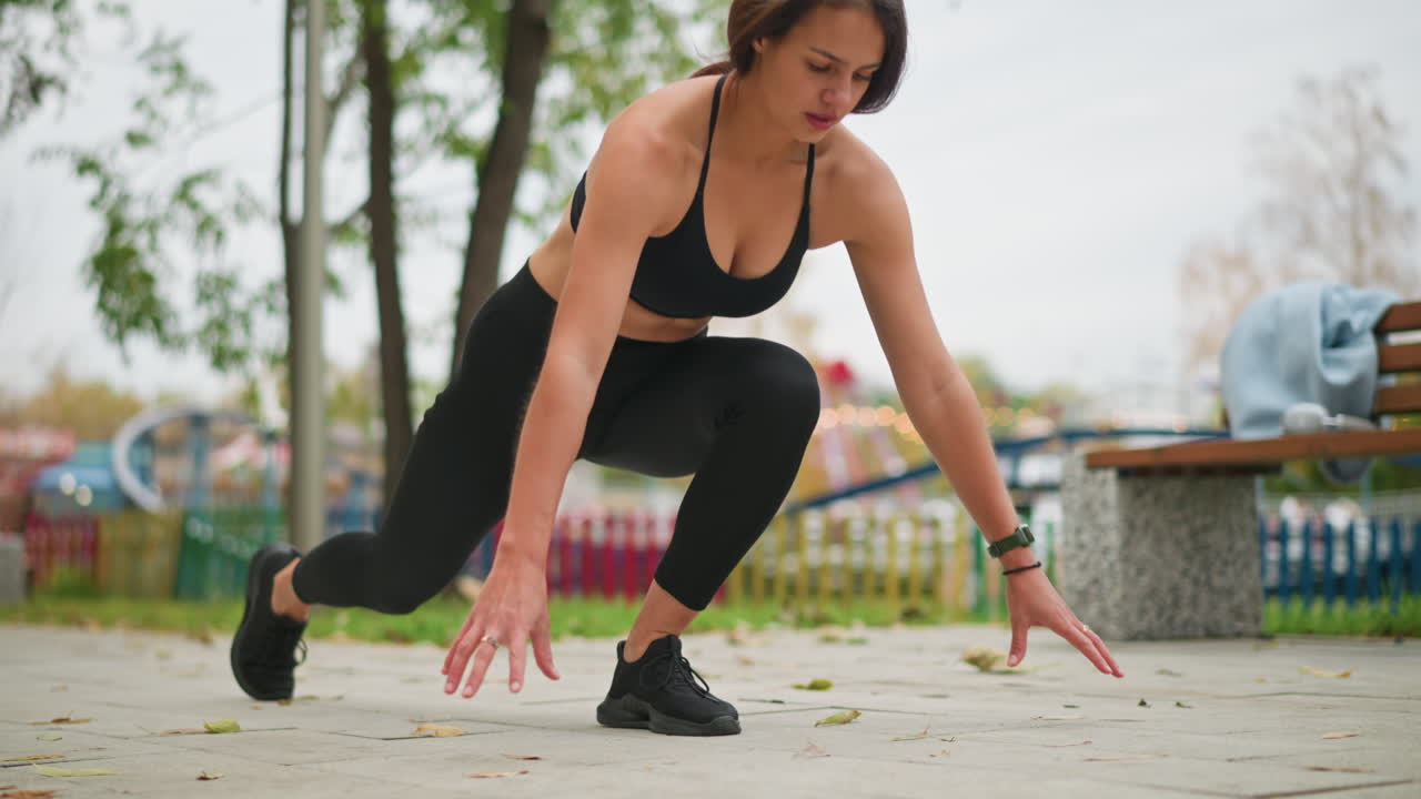 Close view of a lady stretching her leg out, preparing to run in a park, the background features a blurred view of playground games, adding a lively atmosphere to her athletic action