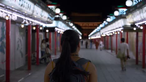 Una-Joven-Viajera-Caminando-Hacia-El-Templo-Sensoji,-En-Cámara-Lenta,-Por-La-Noche-A-Lo-Largo-De-La-Calle-Comercial-Nakamise-En-Asakusa,-Tokio